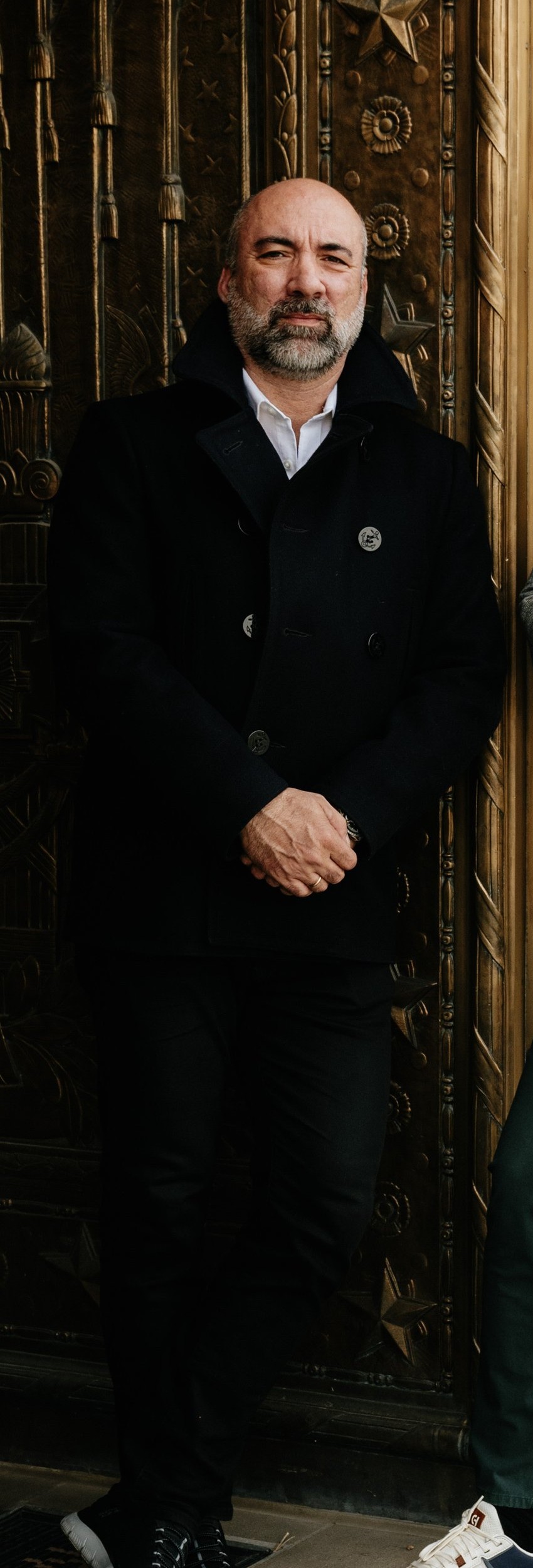 Petar Jankovic — arms crossed, black overcoat, at the doors of the Indianapolis Central Library