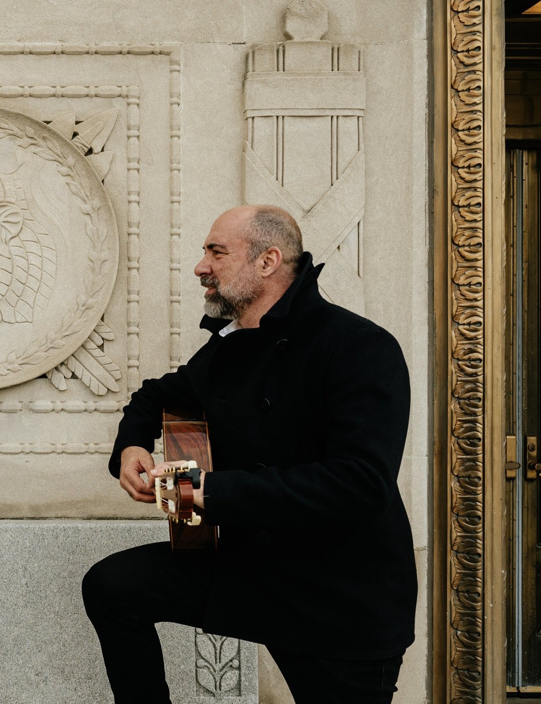 Petar Jankovic in profile, playing guitar next to a carved stone medallion