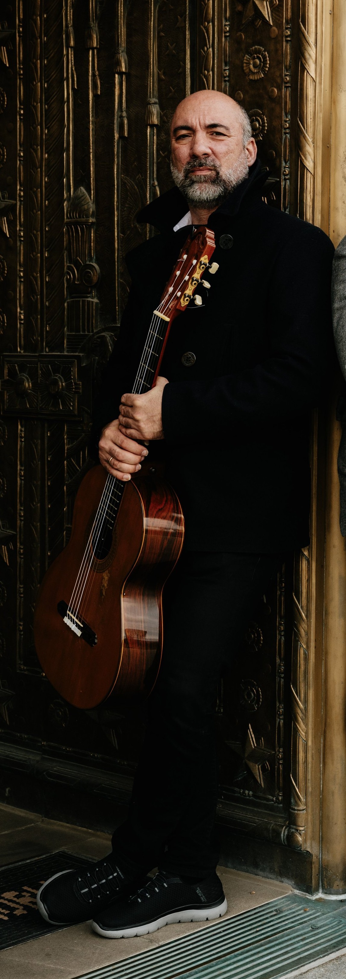 Petar Jankovic standing with his classical guitar in front of ornate bronze doors