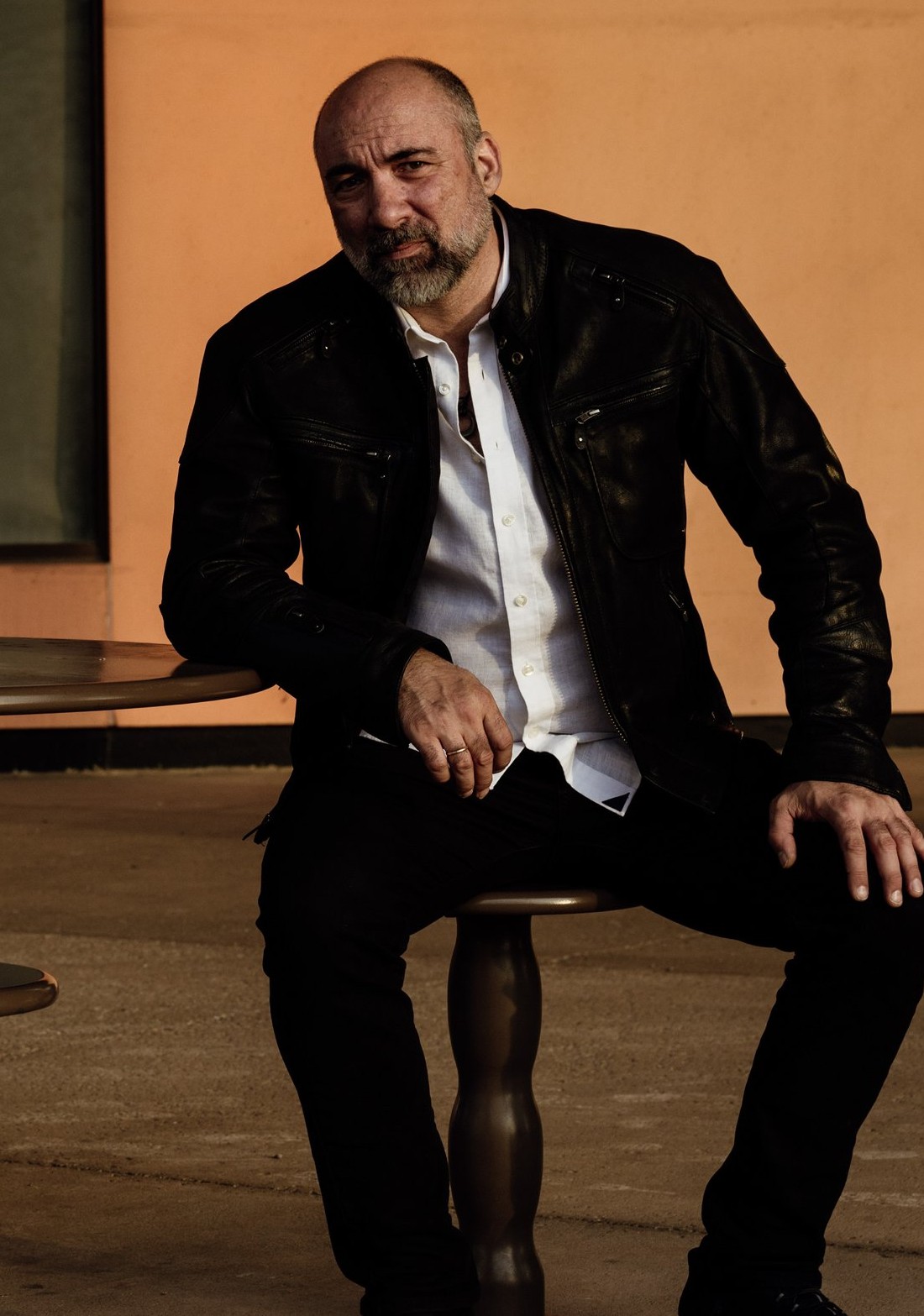 Petar Jankovic seated at a small wooden table, leather jacket, warm orange backdrop