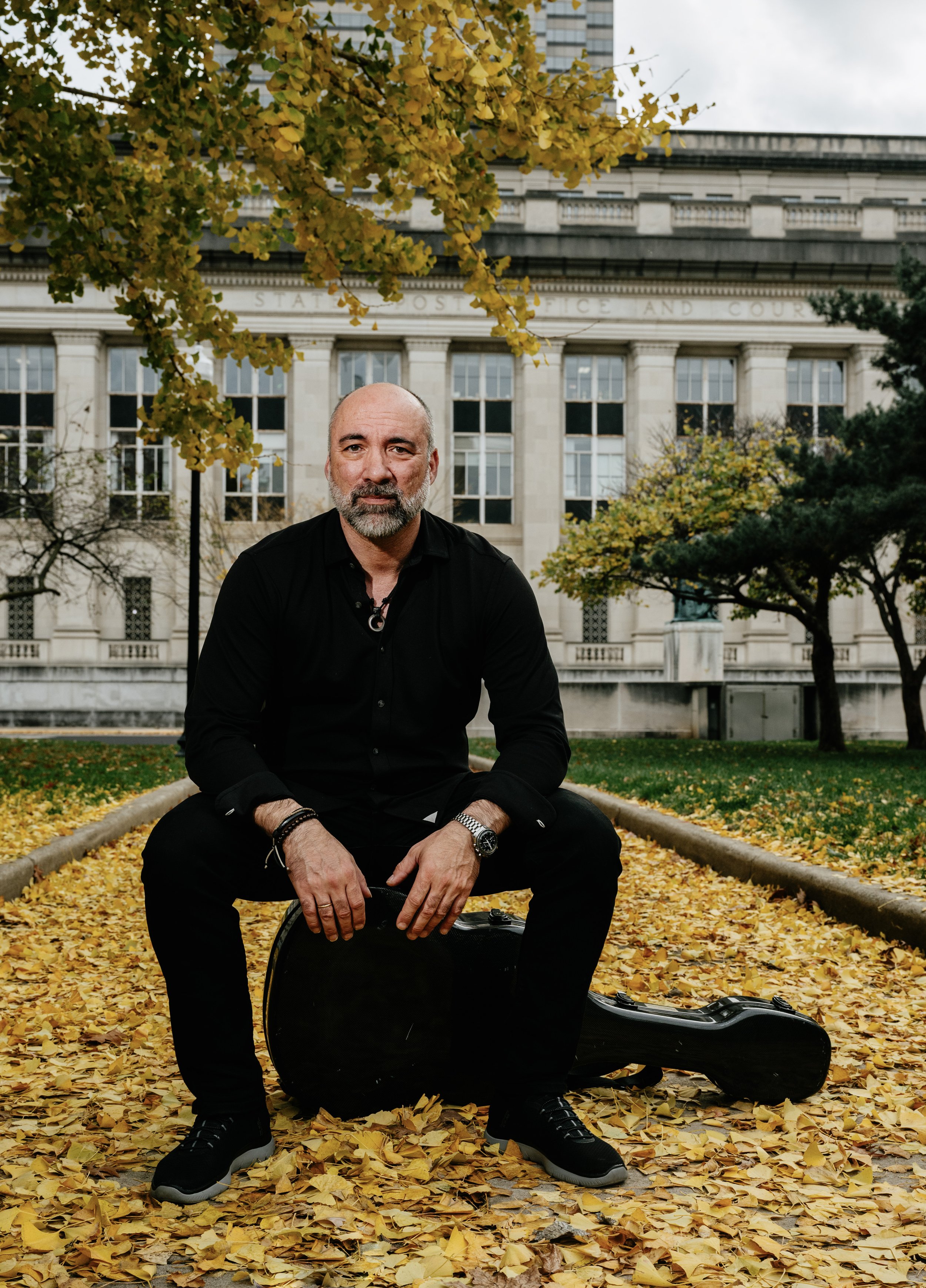 Petar Jankovic seated on his guitar case in golden autumn leaves