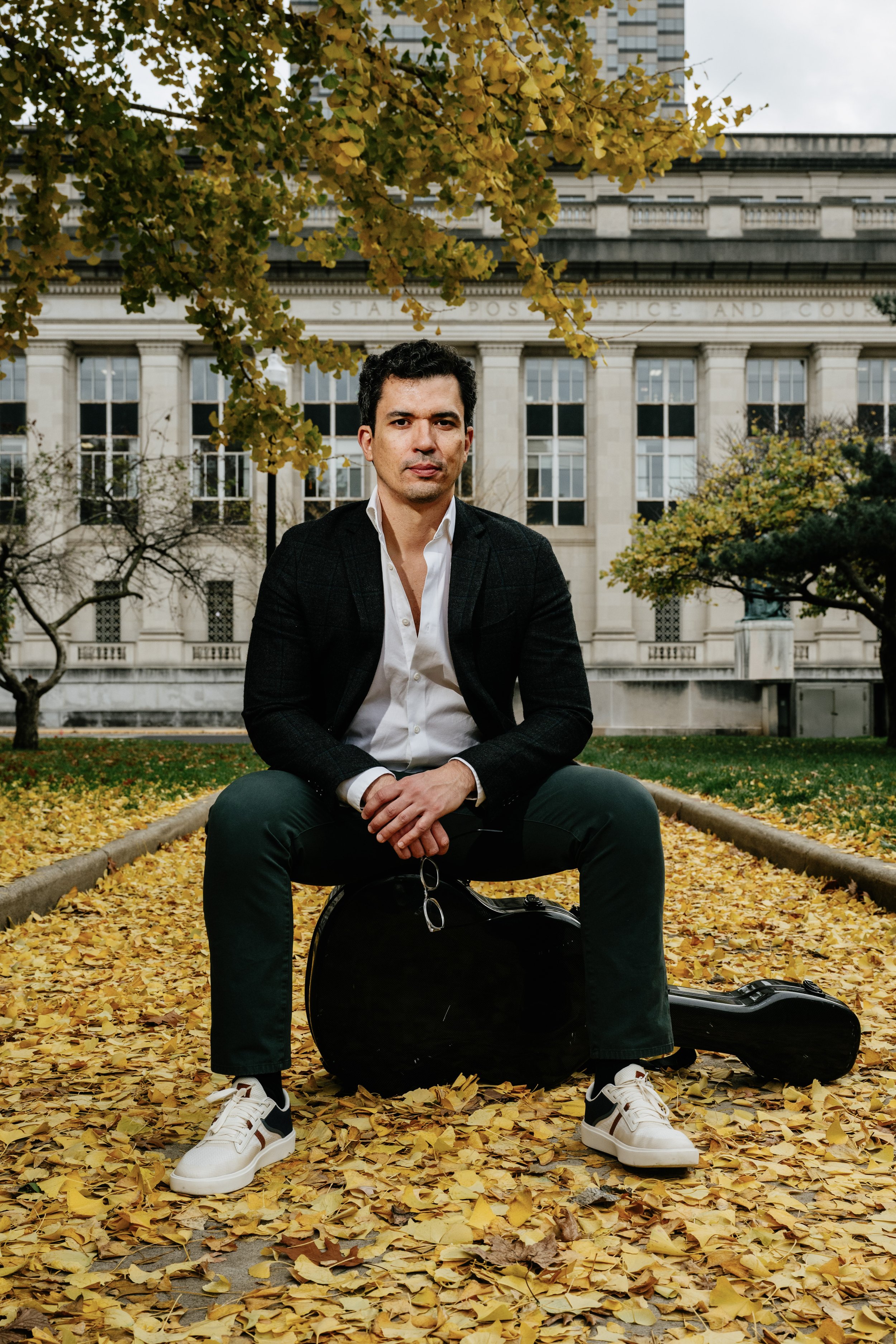 Daniel Duarte — solo portrait seated on a guitar case in autumn leaves